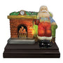 Front view of Santa seated in a green chair beside an illuminated brick fireplace