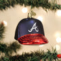 Christmas ornament shaped like a baseball cap with a red brim and blue bill, featuring an Atlanta Braves logo, hanging on a decorated tree.
