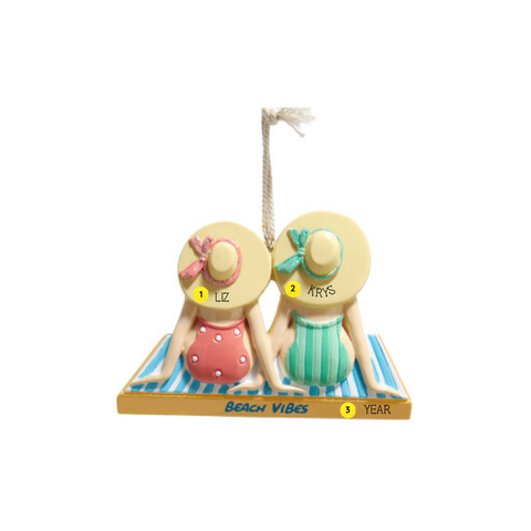 Personalized ornament of two women sitting on striped beach towels in swimsuits and sun hats, with “Beach Vibes” on the front and room for names and year. Shown with example personalization. 