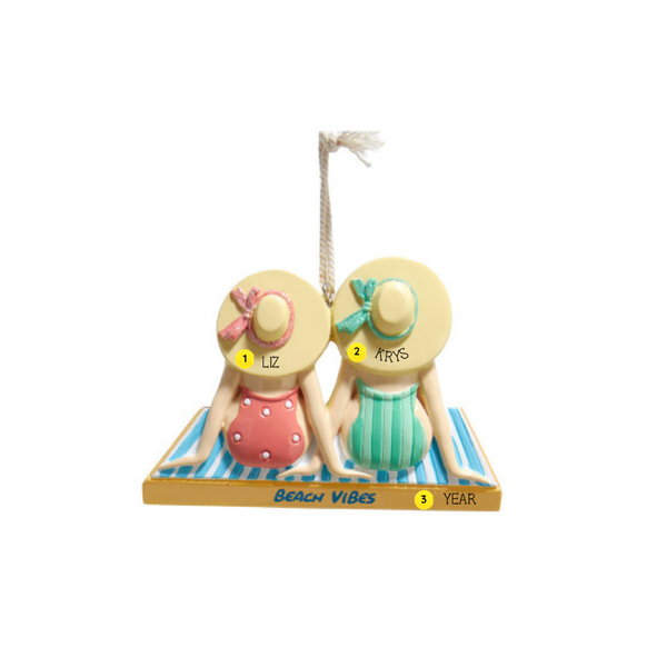 Personalized ornament of two women sitting on striped beach towels in swimsuits and sun hats, with “Beach Vibes” on the front and room for names and year. Shown with example personalization. 