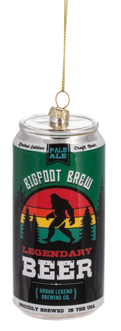 Glass ornament shaped like a beer can labeled “Bigfoot Brew Legendary Beer,” featuring a Bigfoot silhouette with a colorful sunset stripe design.