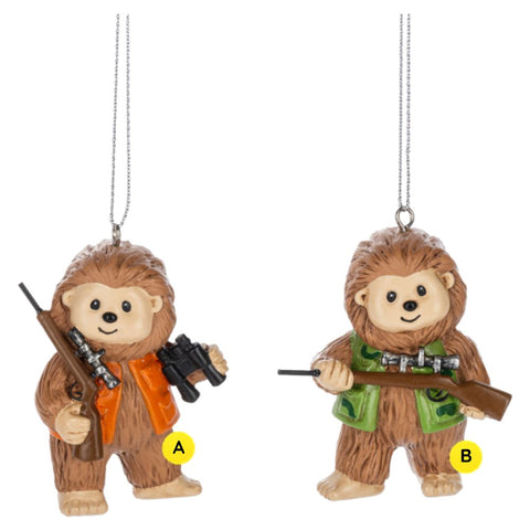 Two Bigfoot Hunting ornaments shown together, each featuring a smiling Bigfoot holding a hunting rifle, with one wearing an orange safety vest and carrying binoculars and the other wearing a green camo-style vest.