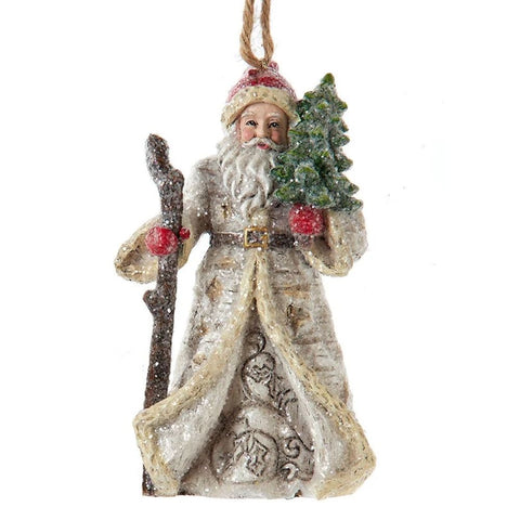 Santa ornament in a textured winter coat with snowy detail, holding a walking staff and decorated evergreen tree in a rustic woodland style.