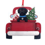 Christmas ornament of a black lab dog in a red truck with a tree and gifts on a white background