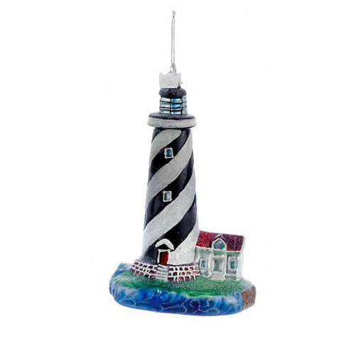 Black and white striped lighthouse ornament with spiral tower design, small coastal cottage, ocean wave base, and silver hanging cord.