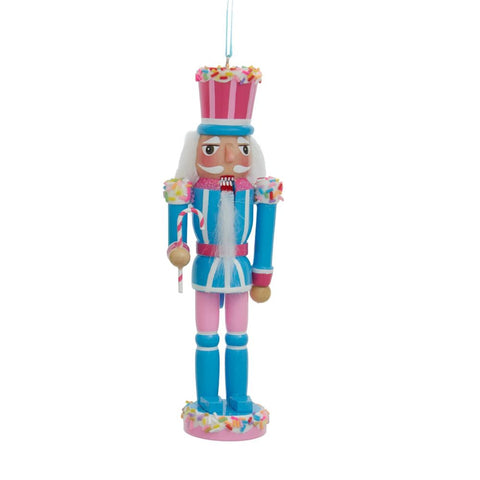 Blue and pink pastel nutcracker ornament with a white beard, sprinkle-covered hat, and small candy cane staff standing on a sprinkled base.