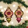 Two pink and gold Christmas ornaments hanging on a tree with blurred lights in the background.