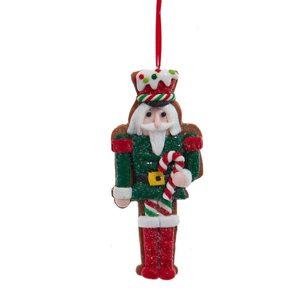 Nutcracker ornament in a green outfit with glittered details, holding a red and white candy cane and wearing a frosting-inspired hat with colorful candy accents.