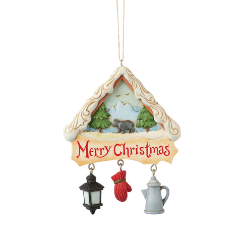 Front view of Jim Shore Christmas at the Lodge Ornament featuring a snowy lodge-shaped design with a bear scene, Merry Christmas message, and dangling winter charms.