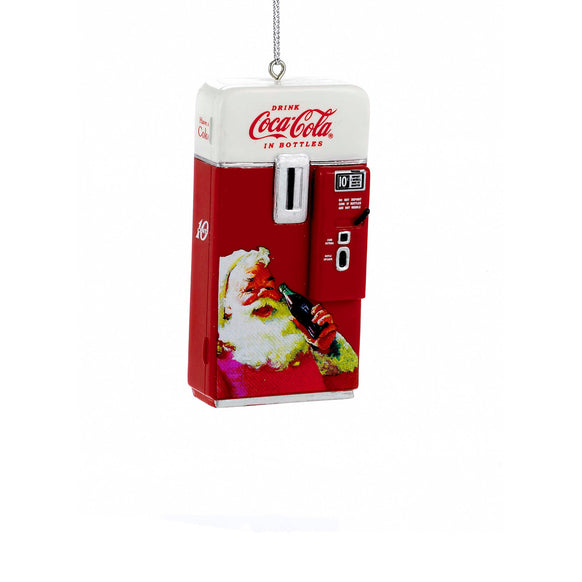 Coca-Cola vending machine ornament in red and white with vintage-style detailing, Coca-Cola logo, coin slot, and Santa holding a bottle on the front.