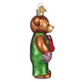 Glass ornament of a corduroy bear in a green dress with a red bag on a white background