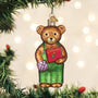 Decorative corduroy bear ornament holding a book, hanging on a Christmas tree with lights in the background.