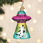 Decorative ornament shaped like a UFO with a cow inside, hanging on a Christmas tree.