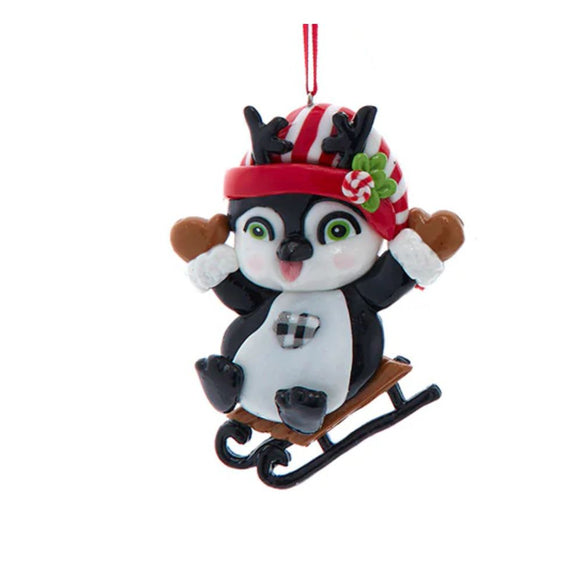 Claydough penguin ornament riding a small sled while wearing a red-and-white striped hat with black antlers.