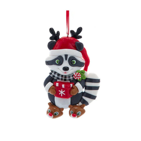 Claydough raccoon ornament wearing a Santa hat with antlers, plaid scarf, and reindeer slippers while holding a red hot cocoa mug.