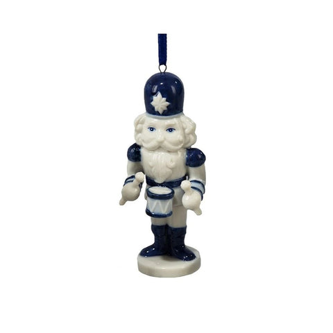 Blue and white nutcracker ornament in a Delft-inspired style holding a drum and drumsticks and standing on a round base with a blue ribbon hanger.