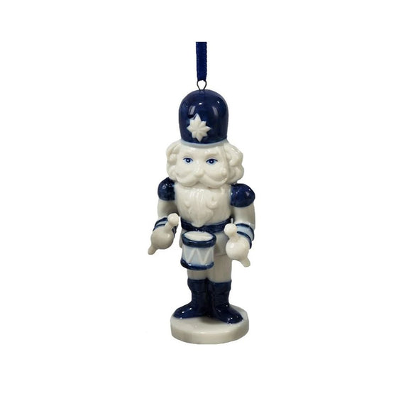 Blue and white nutcracker ornament in a Delft-inspired style holding a drum and drumsticks and standing on a round base with a blue ribbon hanger.