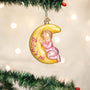 Christmas ornament of a baby on a yellow moon with 'Baby's First Christmas' text, hanging on a decorated tree.