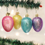 Four glittery Egg Shaped Christmas ornaments in pink, yellow, blue, and purple hanging on a tree branch.
