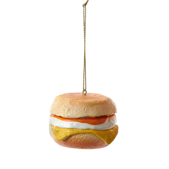 Breakfast sandwich ornament with a round bun, white egg layer, orange topping, and melted yellow cheese hanging from a gold cord.