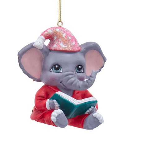 Elephant ornament in red pajamas and a pink glittered nightcap, sitting and reading an open teal book.