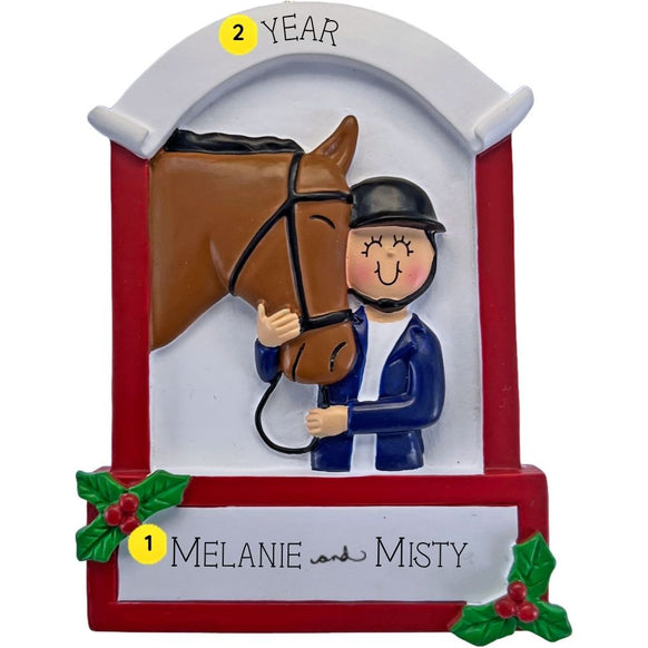 Personalized equestrian ornament featuring a rider in a helmet beside a brown horse, framed by a red and white stable-style design with holly accents. The ornament includes two names and a year.