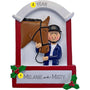 Personalized equestrian ornament featuring a rider in a helmet beside a brown horse, framed by a red and white stable-style design with holly accents. The ornament includes two names and a year.