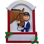 Equestrian ornament featuring a rider in a helmet beside a brown horse, framed by a red and white stable-style design with holly accents. 