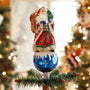 Father Christmas tree topper displayed on top of a decorated Christmas tree with warm lights in the background.