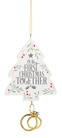 Our First Christmas Together ornament shaped like a white Christmas tree with greenery, red berry accents, and two gold wedding rings hanging below.