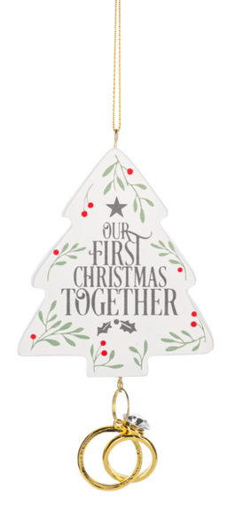 Our First Christmas Together ornament shaped like a white Christmas tree with greenery, red berry accents, and two gold wedding rings hanging below.