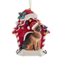 German Shepherd wearing a Santa hat in a red dog house Christmas ornament decorated with colorful lights and holly.