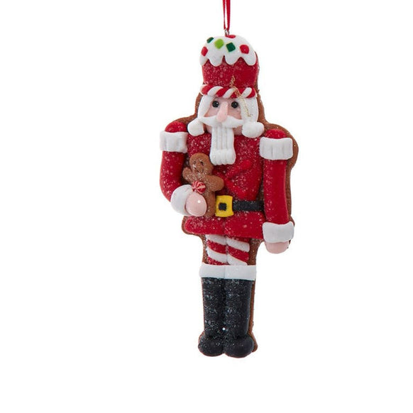 Nutcracker ornament in a red outfit with glittered details, holding a gingerbread cookie and wearing a frosting-inspired hat with colorful candy accents.