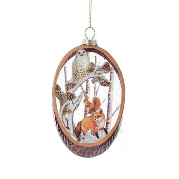 Oval glass ornament featuring a fox, squirrel, owl, and rabbit in a snowy forest scene with pinecones and trees.