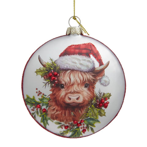 Round glass disc ornament featuring a Highland cow wearing a Santa hat, surrounded by holly leaves, red berries, and glittered festive accents.