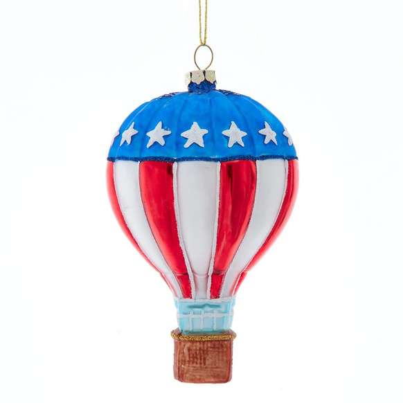 Glass hot air balloon ornament with a blue top, white stars, red and white striped panels, and a brown basket in patriotic colors.