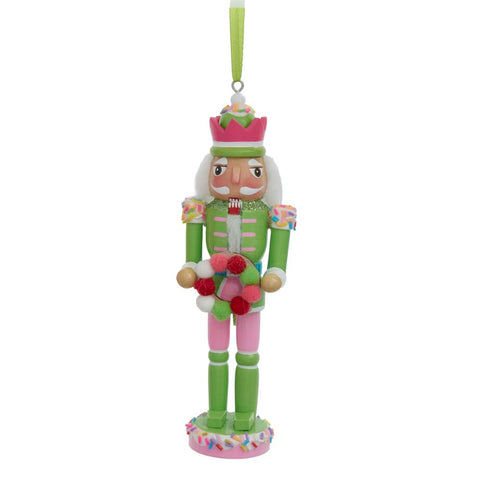Green and pink pastel nutcracker ornament with a white beard, sprinkle-trimmed crown hat, and colorful candy-style wreath on a sprinkled base.