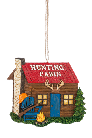 Hunting Cabin ornament featuring a rustic log-style cabin with a red roof, blue door, antlers above the entrance, a campfire, evergreen tree, and Adirondack chair with a hunting rifle.
