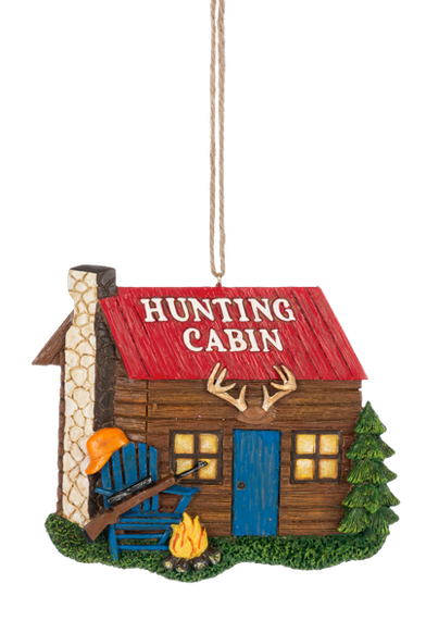 Hunting Cabin ornament featuring a rustic log-style cabin with a red roof, blue door, antlers above the entrance, a campfire, evergreen tree, and Adirondack chair with a hunting rifle.