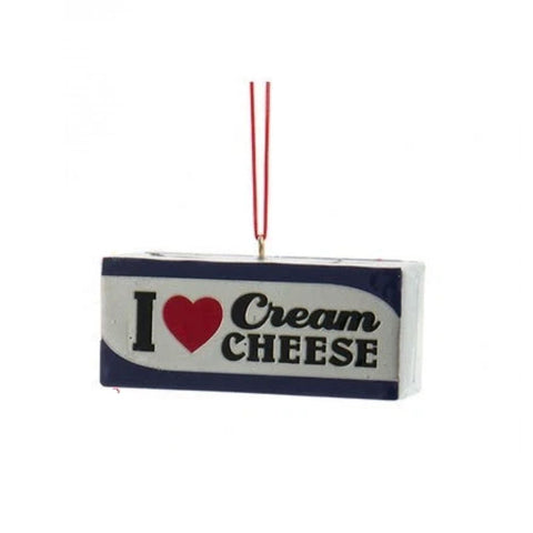Rectangular cream cheese ornament with blue trim and the words “I Love Cream Cheese,” hanging from a red cord.