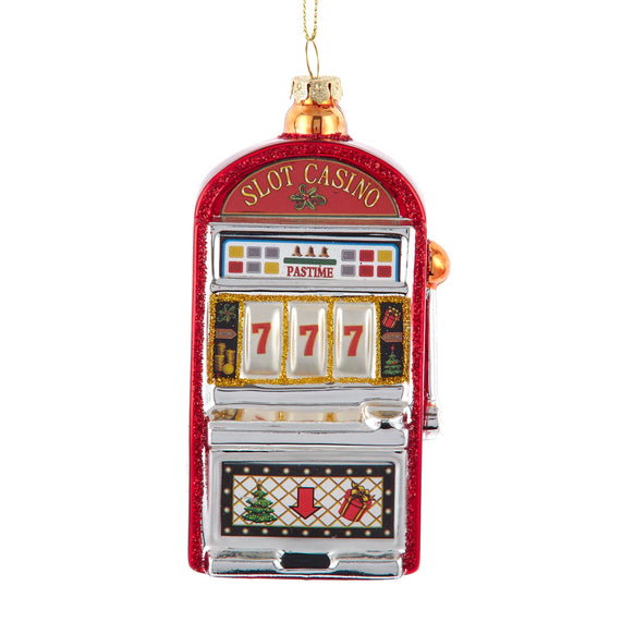 Glass ornament shaped like a red and silver slot machine with glittered trim, a 777 display, and holiday-themed symbols on the front.