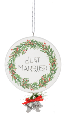 Round white ornament with a green holiday wreath and red berries framing the words “Just Married,” finished with silver bells, greenery, and a red bow at the bottom.