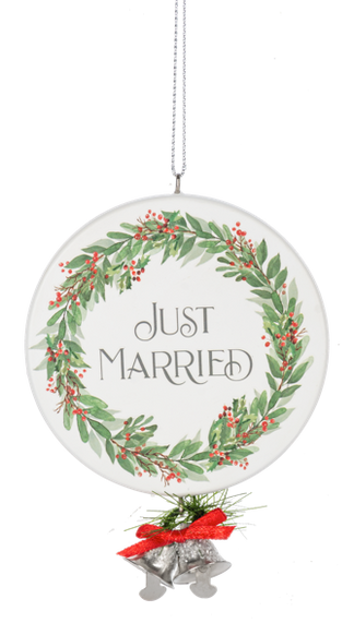 Round white ornament with a green holiday wreath and red berries framing the words “Just Married,” finished with silver bells, greenery, and a red bow at the bottom.