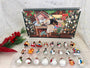 Mini glass ornaments from the advent calendar arranged in a clear tray, showing assorted Santa, snowman, gingerbread, duck, rocking horse, and train designs.