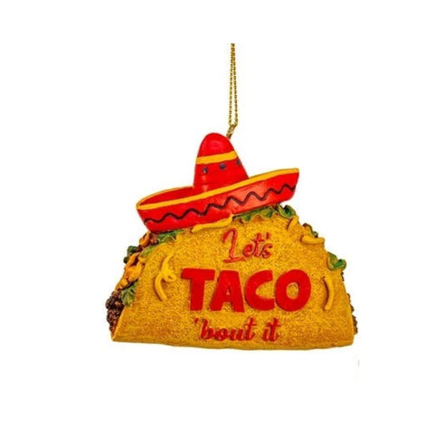 Taco-shaped ornament with the phrase “Let’s Taco ’bout it” and a red sombrero on top, hanging from a gold cord.