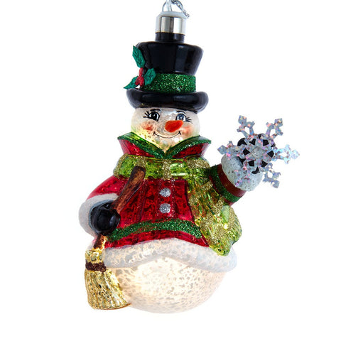 Lighted glass snowman ornament wearing a black top hat, red coat, and green scarf while holding a sparkling snowflake.