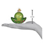 Green glass ornament shaped like a peapod with a face, held in a hand for scale, on a white background.