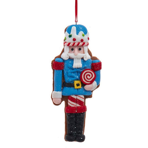 Nutcracker ornament in a blue outfit with glittered details, holding a red and white lollipop and wearing a frosting-inspired hat with colorful candy accents.
