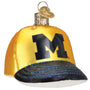 Glass ornament of a yellow baseball cap with a black 'M' for Michigan on a white background