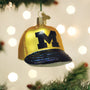 Decorative Christmas ornament shaped like a yellow baseball cap with a black 'M' for Michigan on a blurred festive background.